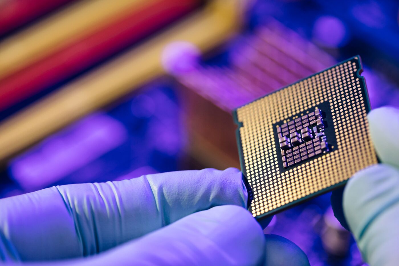 Gloved hands inspecting a microprocessor under colored light